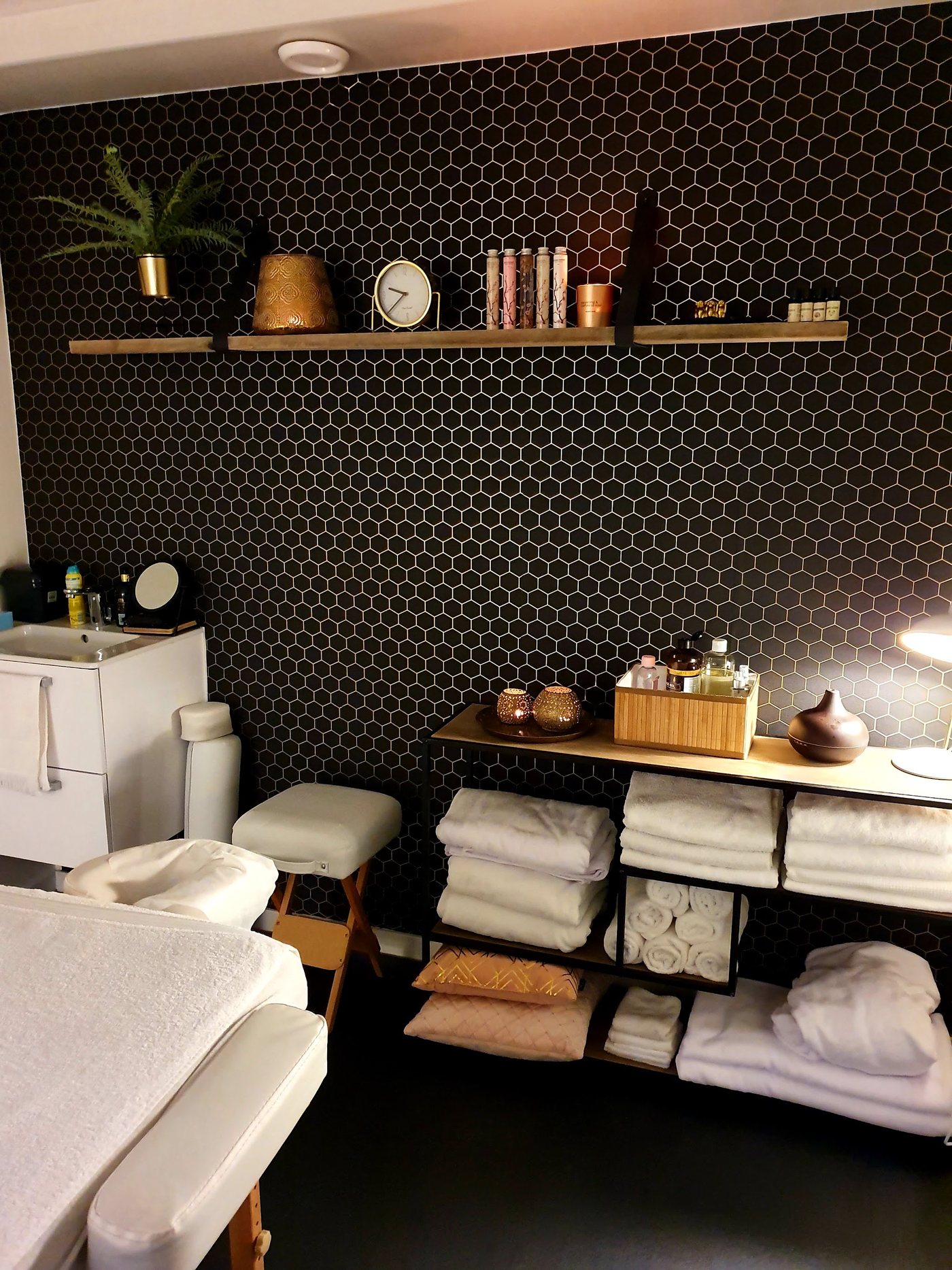De behandelruimte van T.G. Massage Salon: massagetafel, stapels witte handdoeken en kaarsen voor een zwarte tegelwand